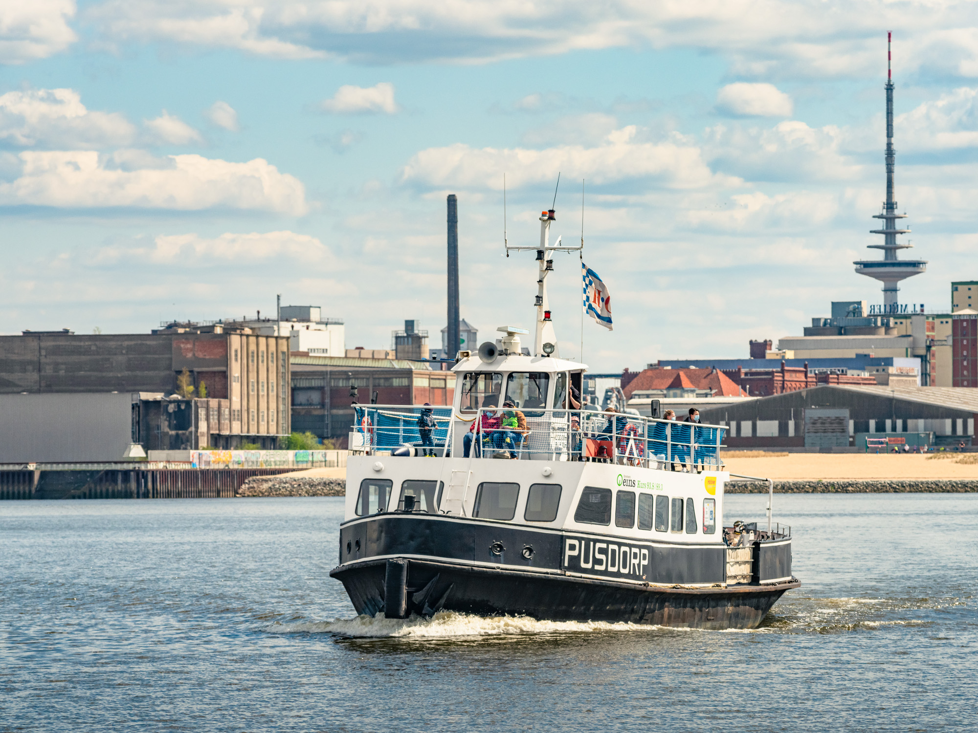 Ein Fahrgastschiff fährt auf dem Fluss. Im Hintergrund ist ein Sandstrand zu sehen, Gebäude und ein Fernsehturm.